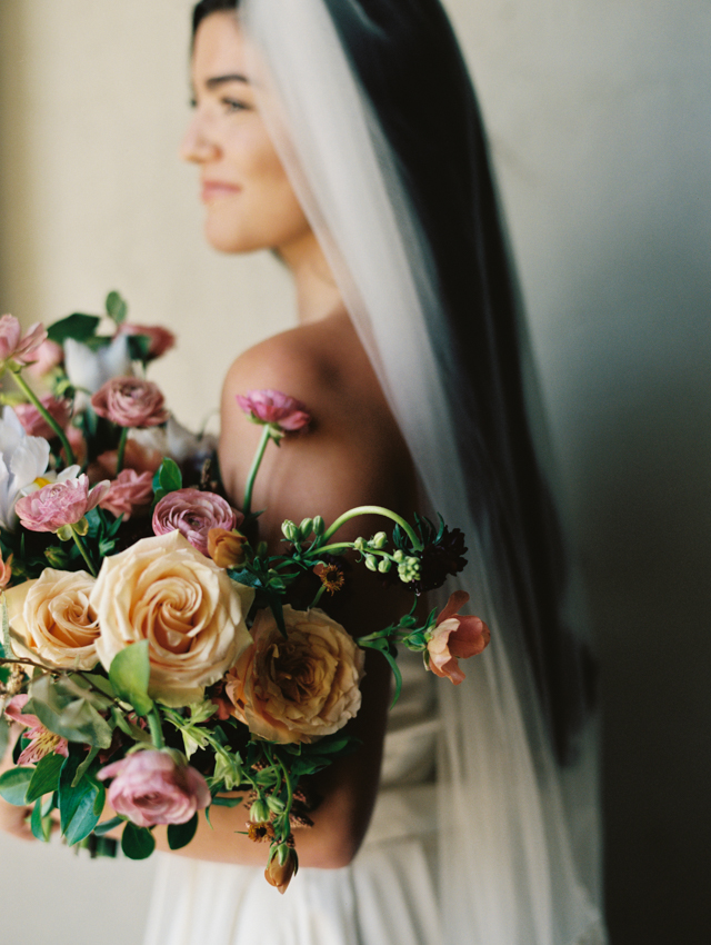 portrait of bride with strapless silk dress, long flowing veil, and lush bridal bouquet